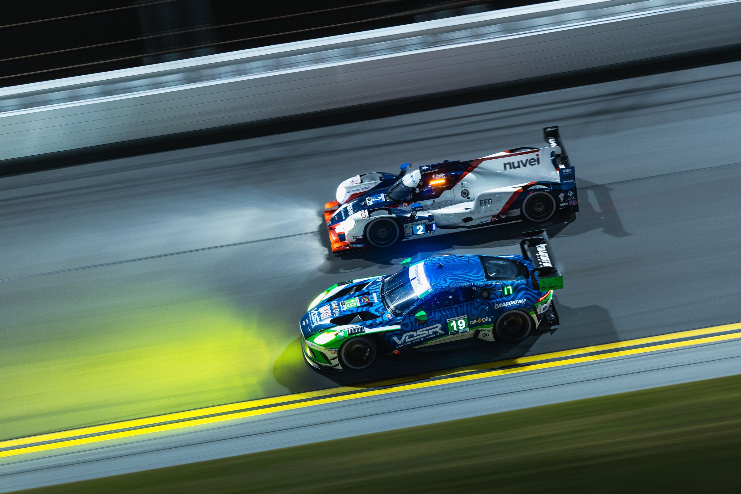 The #19 Van der Steur Racing Aston Martin Vantage GT3 alongside an LMP2 car at night on the Daytona banking